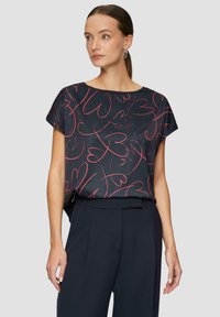 Kurzärmliges navyblaues Oberteil mit rotem Herzmuster; glattes Material; lockere Passform; runder Halsausschnitt; kombiniert mit dunklen, maßgeschneiderten Hosen.