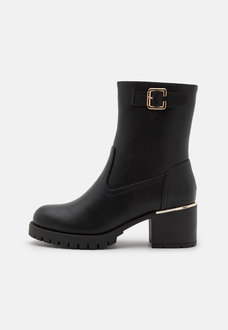 Bottes noires à la cheville en matériau synthétique texturé. Présentent un détail de boucle dorée, un talon épais et une semelle en caoutchouc avec des crampons.