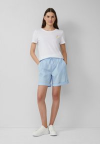 T-shirt en coton blanc avec une petite broderie de banane jaune, associée à un short bleu clair avec une taille élastique et des manches retournées.