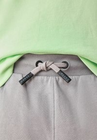 Lichtgroene geribbelde t-shirt gelaagd over grijze joggingbroek met een trekkoord met zwarte accenten en een geknoopte afwerking.
