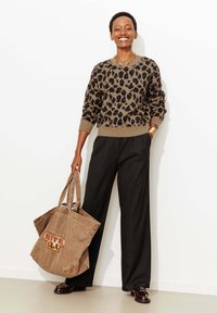 Pull imprimé léopard en beige et noir, associé à un pantalon taille haute noir. Tient un grand sac fourre-tout marron avec un logo. Des mocassins marron complètent la tenue.