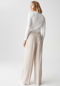 Crème lange mouw top met een naaddetail aan de achterkant, gedragen met lichtbeige wijde broek met een zachte textuur en elastische tailleband.