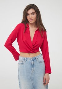 Cropped top rosso con scollatura profonda e maniche lunghe, realizzato in un tessuto morbido. Abbinato a una gonna in denim azzurra a vita alta.