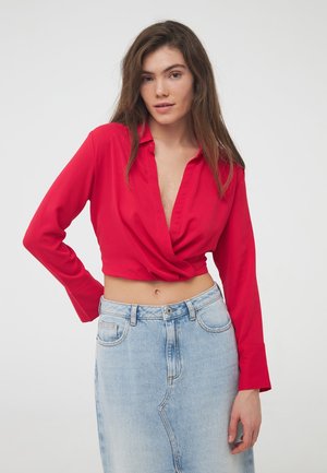 Cropped top rosso con scollatura profonda e maniche lunghe, realizzato in un tessuto morbido. Abbinato a una gonna in denim azzurra a vita alta.