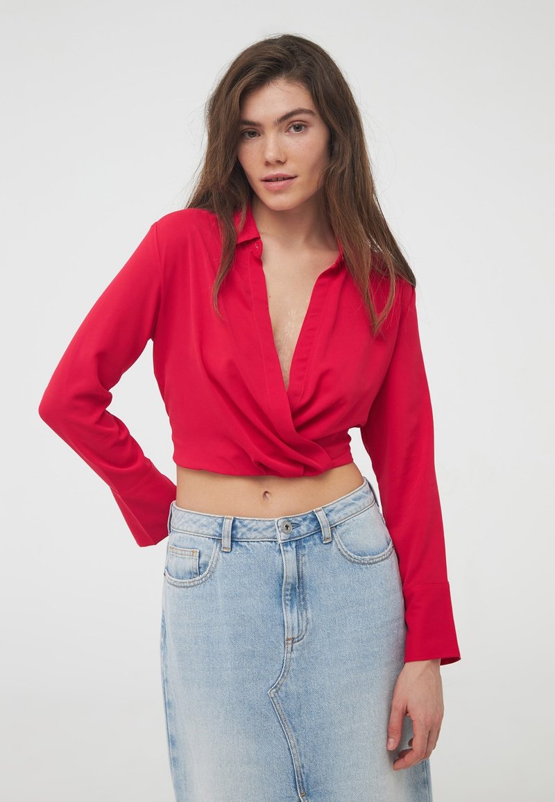 Cropped top rosso con scollatura profonda e maniche lunghe, realizzato in un tessuto morbido. Abbinato a una gonna in denim azzurra a vita alta.