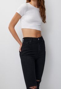 T-shirt blanc court à manches courtes associé à un jean en denim noir taille haute avec des déchirures près des genoux.