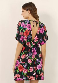 Abito floreale con grandi fiori rosa, rossi e viola su uno sfondo nero, dotato di una profonda scollatura a V sul retro e maniche corte e larghe.