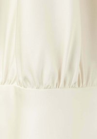 Gros plan d'un tissu blanc avec des coutures rassemblées le long d'une couture créant des plis doux et des détails de texture.