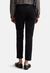 Zwarte corduroybroek met een tapered fit, twee achterzakken en een gladde textuur. Draagt met zwarte ballerina's en een gestreepte longsleeve.