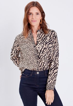 Blouse imprimé léopard avec un mélange de couleurs noire et beige, manches longues, col et fermeture à boutons, associée à un jean en denim foncé.