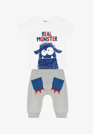 Weißes T-Shirt mit kurzen Ärmeln und blauer Monster-Grafik sowie dem Text "REAL MONSTER". Graue Hose mit blauen Taschen und roten Akzenten in Form von Stacheln.