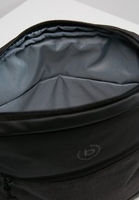 Zaino in tessuto nero con un interno grigio liscio. Presenta un'apertura con zip e un logo circolare all'esterno.