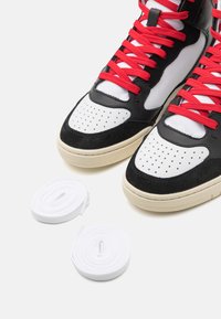 Černobílé kožené vysoké tenisky s červenými tkaničkami, perforovanou špičkou, texturovanými semišovými akcenty a dvěma náhradními bílými tkaničkami.