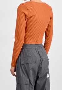 Top de manga larga ceñido con canalé en color naranja quemado, combinado con pantalones cargo grises que cuentan con múltiples bolsillos y cinturilla elástica.