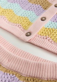 Prim-plan al unui cardigan tricotat în culori pastel, cu modele galbene, lavandă și mentă, margine roz cu nervuri și nasturi maro pe partea din față.