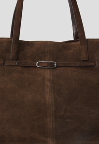 Borsa a spalla in suede marrone con due manici lunghi, un dettaglio di cintura piatta e un accento in fibbia ovale argentata sul davanti.