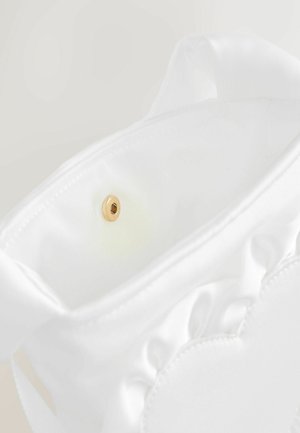 Gros plan sur un sac en tissu blanc avec une fermeture à pression magnétique dorée à l'intérieur de l'ouverture.