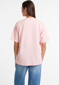 Lys pink bomulds T-shirt med en afslappet pasform, korte ærmer og rund halsudskæring. Bagfra viser den en glat, ufærdig overflade.