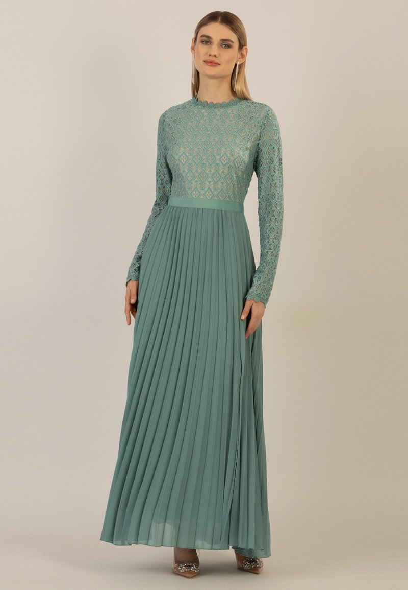 Lungo abito turchese con corpetto in pizzo a motivo diamante, gonna plissettata, maniche lunghe e una silhouette elegante.