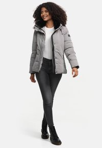 Grijze pufferjack met een afneembare zwart bont gevoerde capuchon, een ritssluiting aan de voorkant en geribbelde manchetten, gecombineerd met zwarte skinny jeans en veterschoenen.