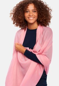 Châle rose clair en tissu doux, drapé sur un haut bleu foncé, présentant une texture lisse et un design fluide, idéal pour le superposition.