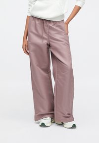 Helle rosa weit geschnittene Hosen mit Kordelzug in der Taille und Seitentaschen, aus glattem, synthetischem Material, kombiniert mit weißen Turnschuhen.