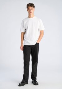 Maglietta bianca a maniche corte abbinata a pantaloni neri e scarpe nere. Il tessuto sembra liscio; l'outfit presenta un design classico e semplice.