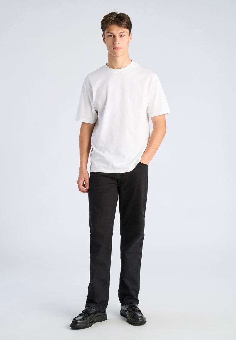 Maglietta bianca a maniche corte abbinata a pantaloni neri e scarpe nere. Il tessuto sembra liscio; l'outfit presenta un design classico e semplice.