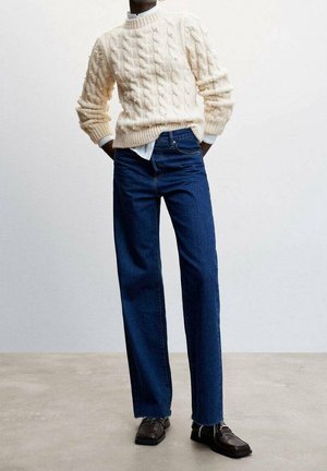 Cremefarbener, kabelgestrickter Pullover kombiniert mit hoch taillierten, gerade geschnittenen blauen Jeans und dunkelbraunen Loafers. Strukturierter Stoff und lockere Passform.