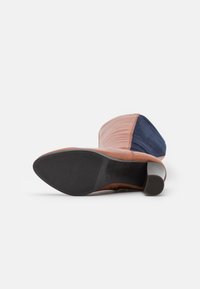 Brown leather boot with a navy blue fabric panel, elevated heel, and textured rubber sole featuring vertical grooves for grip.