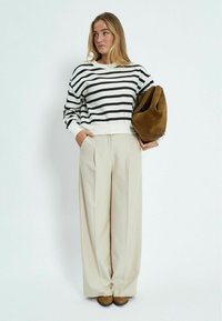 Crna i bijela prugasta dukserica s rebrastim rukavima, uparenih s bež hlačama širokih nogavica visokog struka i smeškim suedom torbom.