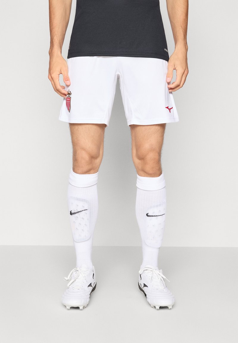 Vita fotbollsshorts med röda accenter och logotyp; svart träningsskjorta; vita strumpor med svart Nike-logotyp; vita fotbollsskor med svarta detaljer.