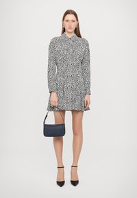 Black and white patterned dress with long sleeves, collar, and flared skirt; paired with a small navy handbag and black heels.