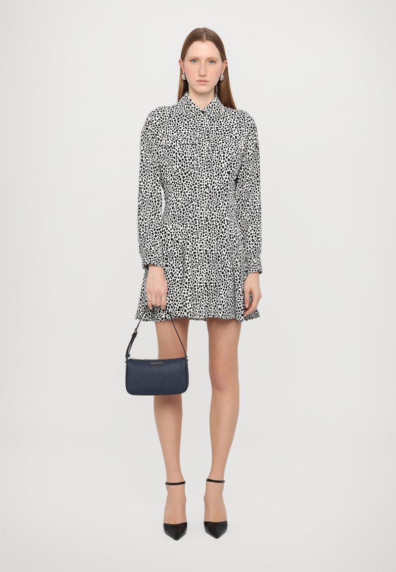 Black and white patterned dress with long sleeves, collar, and flared skirt; paired with a small navy handbag and black heels.