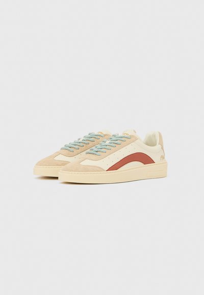 Beige suède en crème kleurige lederen sneakers met een rood gebogen ontwerp en lichtblauwe veters. Gestructureerde bovenkant, platte zool en merkdetails op de hiel.