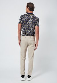 Polo bleu marine à motif floral, pantalon beige ajusté et baskets noires avec semelles blanches, vues de derrière sur un fond clair.