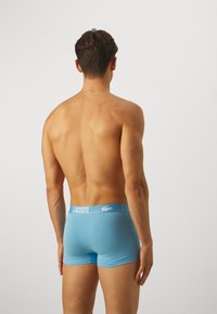 Blue cotton boxer shorts with a white Lacoste logo waistband, featuring a fitted design and smooth texture, viewed from the back.