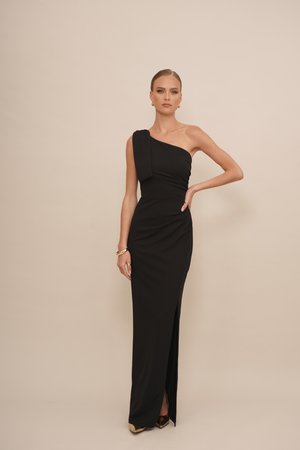 Robe de soirée noire à une épaule, avec un tissu froncé, une fente sur le côté et une silhouette élancée. Accentuée par des bijoux en acier inoxydable doré simples.
