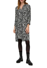 Schwarz-weißes Zebra-Musterkleid mit langen Ärmeln, V-Ausschnitt und einem leichten Fall. Kombiniert mit schwarzen Stiefeletten und Strumpfhosen.