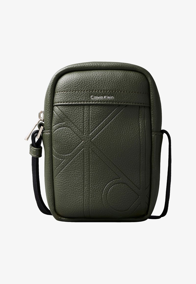 Μικρή τσάντα Calvin Klein σε ελιά πράσινο χρώμα, με ανάγλυφα μεγάλα αρχικά και μαύρο ρυθμιζόμενο λουρί, κλείσιμο με φερμουάρ στην αριστερή πλευρά.