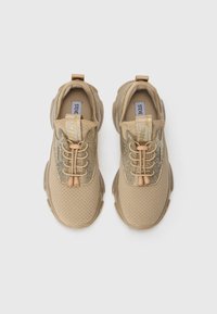 Et par beige nettosneakers med elastiske skolisser og glitrende sidepaneler, sett ovenfra på en hvit bakgrunn.