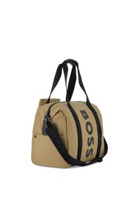 Borsa da viaggio rettangolare tan con manici neri e grande testo verticale "BOSS", dotata di una tasca laterale e una tracolla rimovibile.