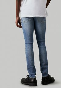 Jeans ajustados de color azul claro con textura desgastada, cinco bolsillos y yugo trasero. Combinados con zapatos negros de cordones y una camiseta blanca.