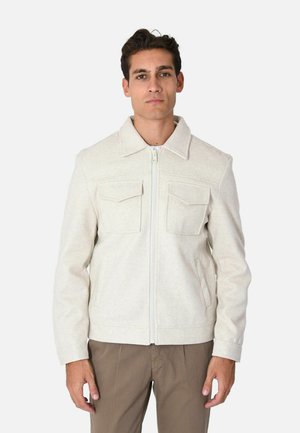 Giacca zip-up beige chiaro realizzata in tessuto testurizzato, con colletto, due tasche sul petto e maniche lunghe. Abbinata a pantaloni beige.