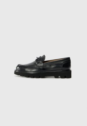 Black leather loafers with a rounded toe, decorative buckle accent, and textured rubber sole. Smooth surface with contrast stitching details.