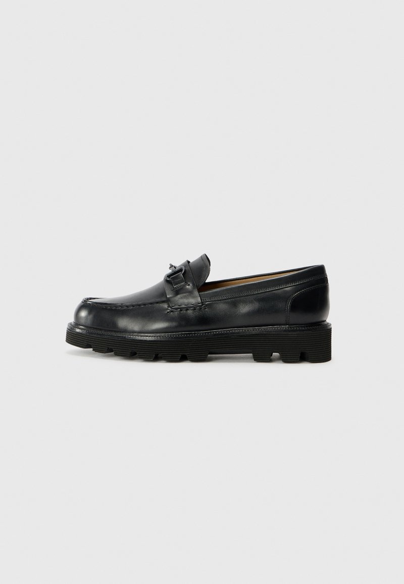 Black leather loafers with a rounded toe, decorative buckle accent, and textured rubber sole. Smooth surface with contrast stitching details.