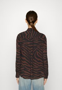 Long-sleeve shirt in black and brown tiger stripe pattern, made of lightweight fabric. Features a classic collar and buttoned cuffs.