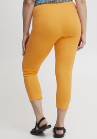 Oranžové capri legíny vyrobené z pružného materiálu, s těsným střihem a hladkou texturou, končící těsně pod lýtkem.