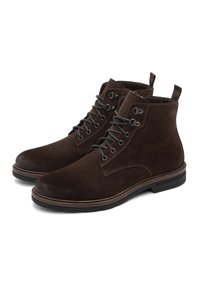 Un paio di stivali alla caviglia in camoscio marrone scuro con suole nere e occhielli in metallo, progettati per un look casual o formale.
