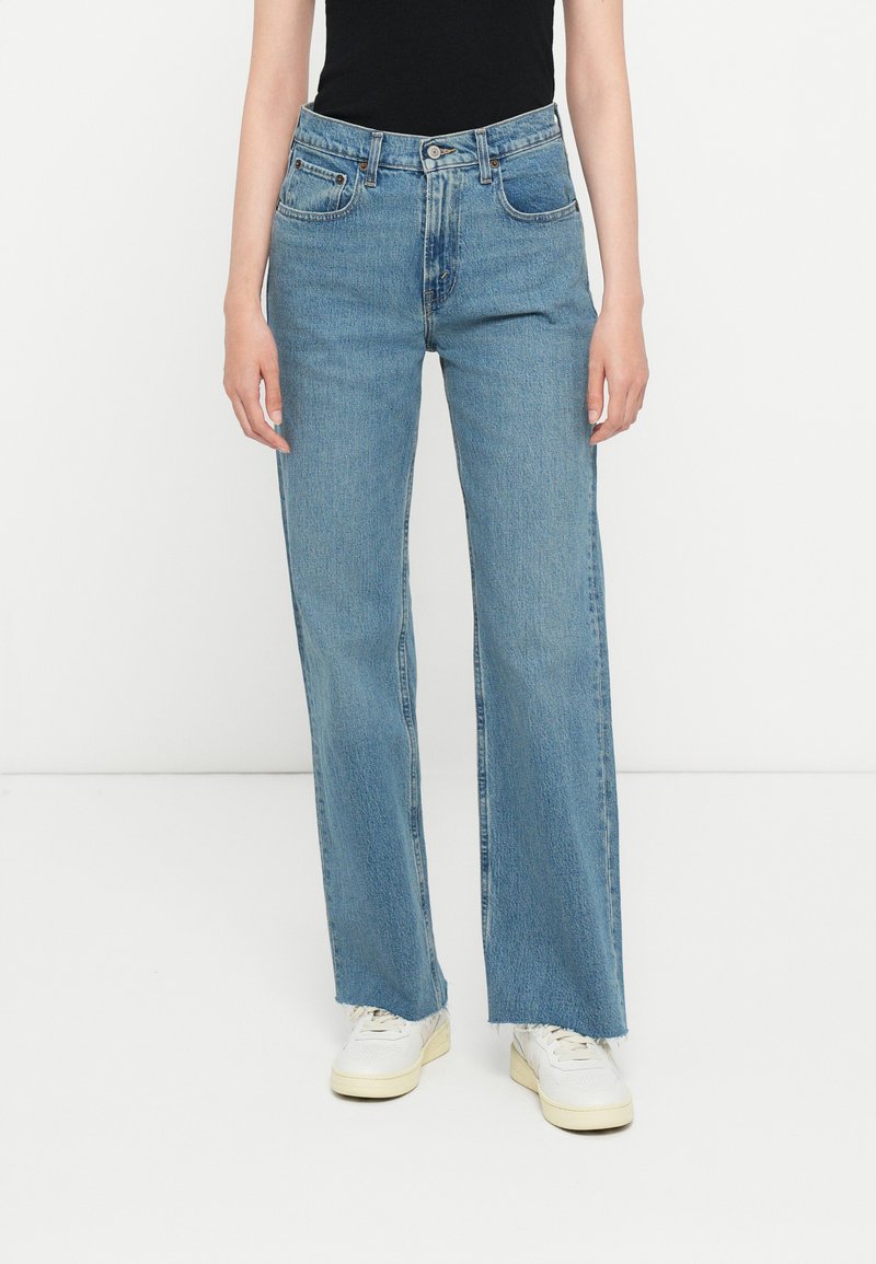 Ανοιχτό μπλε τζιν παντελόνι με ίσια γραμμή, που διαθέτει ψηλή μέση, σχέδιο με πέντε τσέπες και ραμμένο στρίφωμα. Συνδυασμένο με λευκά αθλητικά παπούτσια.